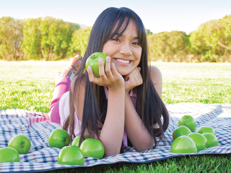 A young lady outside on a blanket holding and apple.